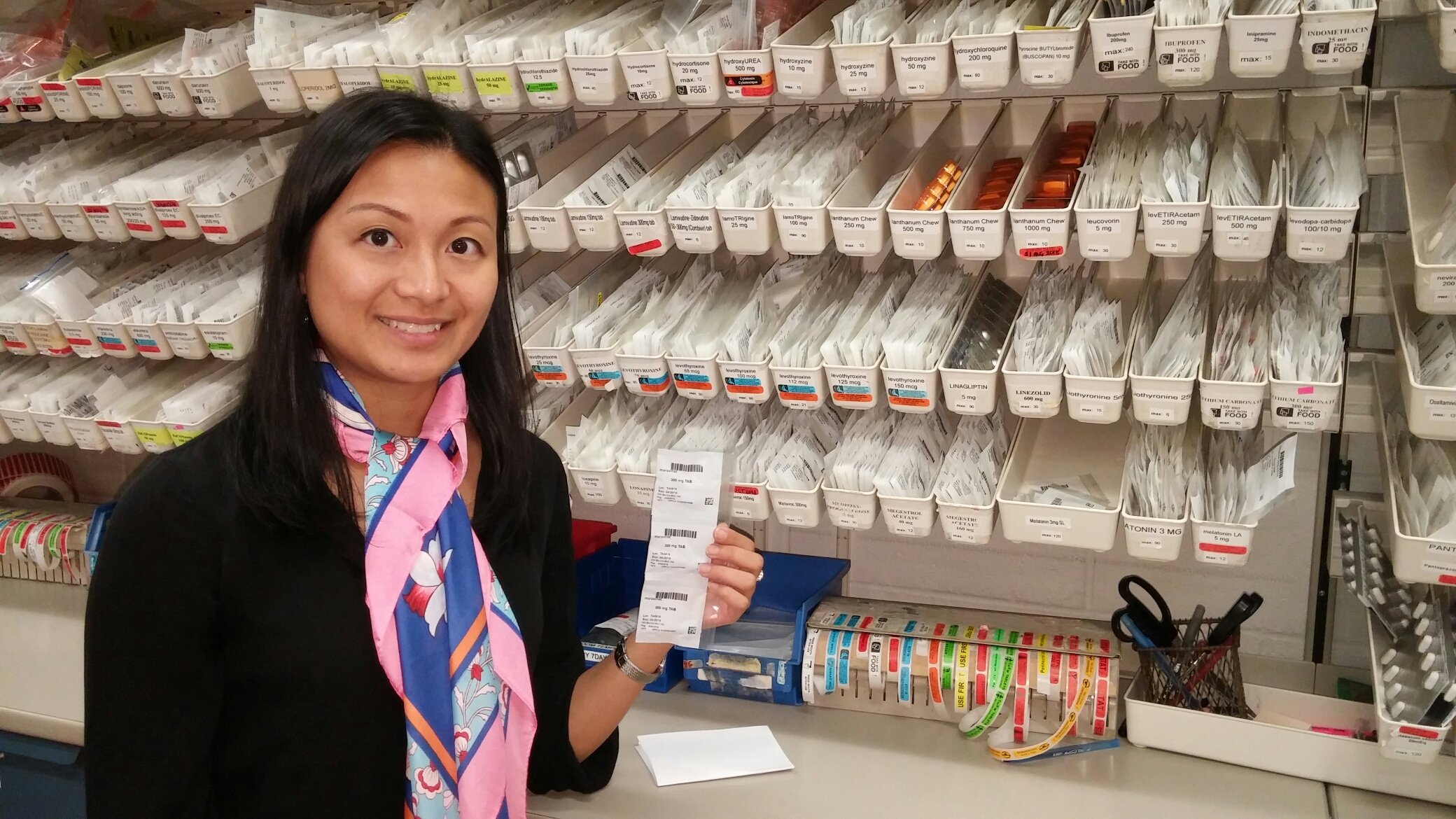 Photo of Winnie Ma in front of pharmacy shelves.