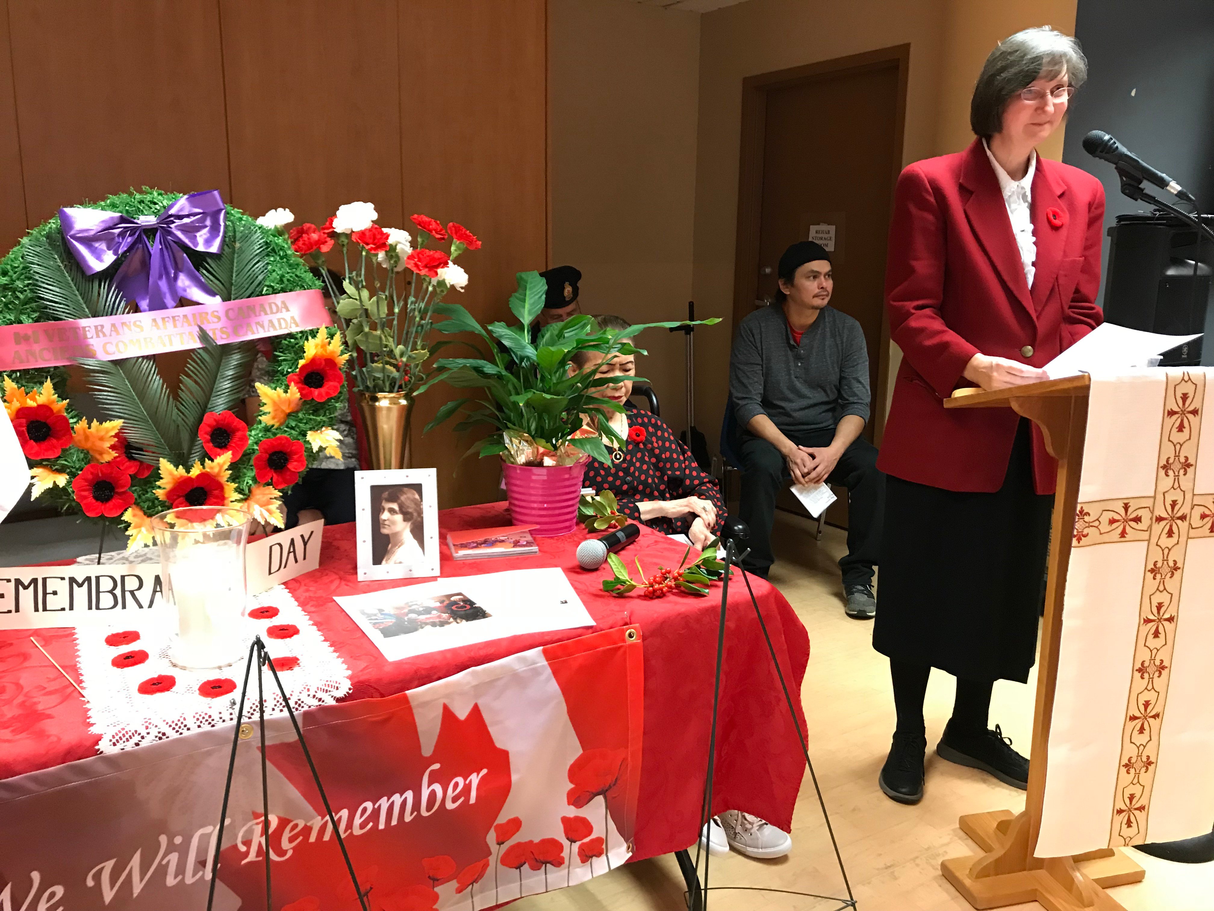 Cecilia Moore at podium with table of Remembrance Day wreaths next to her.