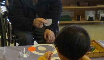 Youville resident sits with child from the Montessori school, doing an activity together.