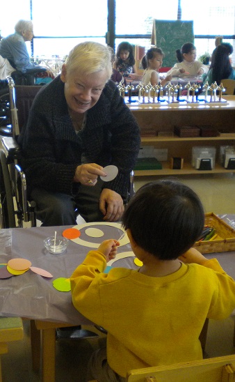 Youville resident sits with child from the Montessori school, doing an activity together.