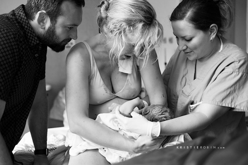 New mother holds her baby just after birth, with support from midwife, Katharina Prass-Aksu (R) from Bloom Midwives.