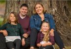 Hayley Atkinson, kidney transplant recipient, sitting in front of tree with husband Bill and two daughters.
