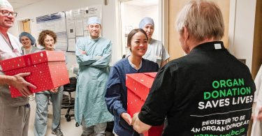 Nurse from OR reaching out to receive box of popcorn from kidney recipient.