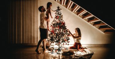 Family gathered around a tree with lights, child placing star on tree