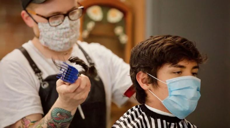 A Victoria, B.C., barber and client both wear masks during a haircut in May after provincial officials made them mandatory for hair salons to reopen. (Photo credits: Michael McArthur/ CBC News)