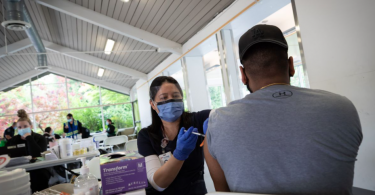 Femia Gabiana, a licensed practical nurse at B.C.'s Fraser Health region, administers a first dose of Pfizer vaccine at a walk-in vaccination clinic at Bear Creek Park in Surrey, B.C. (Photo credit: The Globe and Mail)