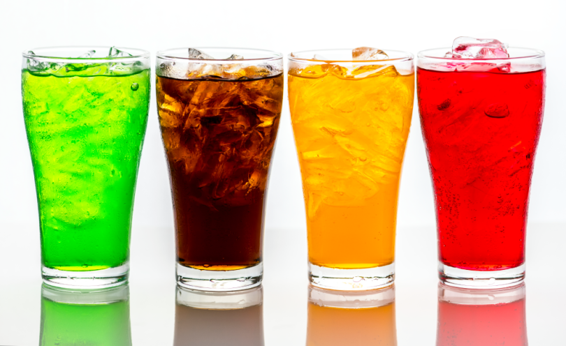 Four glasses filled with sugary drinks of different colours.