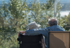 Two seniors with their backs turned to the camera sit outside looking at waterfront.