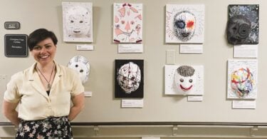 An art therapist stands by a display of eight colourful masks made by patients at Providence Health Care.