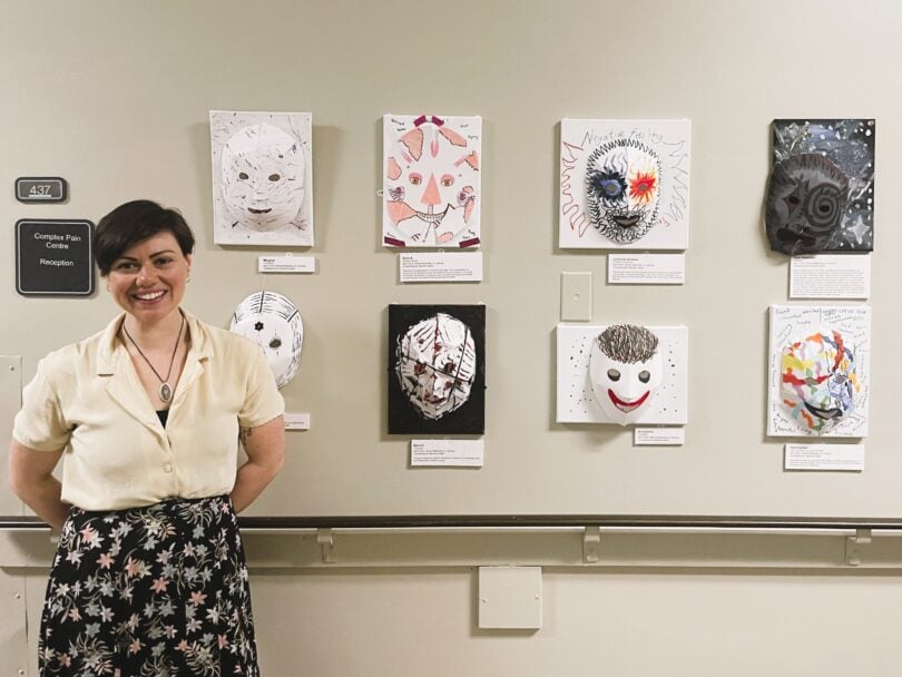 An art therapist stands by a display of eight colourful masks made by patients at Providence Health Care.
