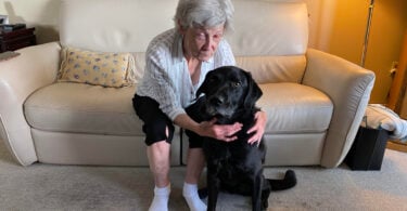 Woman smiling at black lab guide dog after regaining partial sight